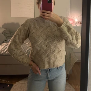 Beige stickad tröja - Säljer en supermysig beige stickad tröja med ett snyggt flätmönster. Tröjan har långa ärmar och en ribbad kant vid ärmslut och nederkant. Den är både varm och stilren. Från Nakd strl S/M