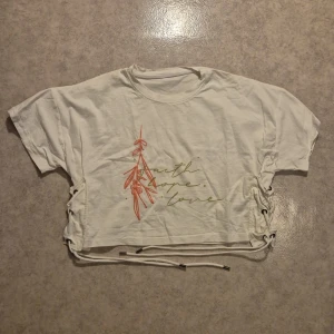 Cropped tröja med tryck - Vit cropped tröja med tryck och snörning i sidan, aldrig använd, storlek står ej i plagget men gissar på M