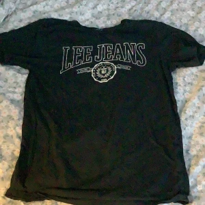 Svart t-shirt från Lee Jeans - Säljer en svart t-shirt från Lee Jeans i storlek S. Den har ett stort tryck med 'Lee Jeans' på framsidan. Perfekt för en avslappnad stil och passar till vardags. T-shirten är i bomull och har en normal passform.