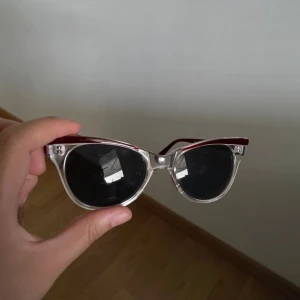 Snygga solglasögon med röd och transparent båge - Coola solglasögon med en unik design! De har en röd överdel och transparenta bågar som ger en modern look. Perfekta för soliga dagar och att matcha med sommaroutfits. Glasen är mörka och skyddar bra mot solen. Ett måste för alla som vill sticka ut i mängden!