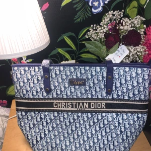 Blå och vit shoppingväska - Säljer en snygg och rymlig shoppingväska i blått och vitt med deras ikoniska mönster. Väskan har ett brett band med logotypen och är perfekt för både vardag och shoppingrundor. Insidan är fodrad med ett mönster och har gott om plats för alla dina saker. Perfekt för dig som vill ha stil och funktion i ett!