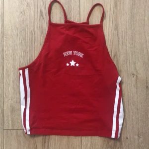 Röd linne från H&M Divided - Säljer ett snyggt rött linne från H&M Divided med texten 'New York' och stjärnor på framsidan. Linnet har smala axelband och vita ränder på sidorna. Perfekt för sommardagar eller en sportig look. Mycket bra skick!