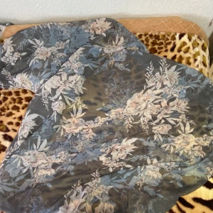 Blommig slöja - Säljer en superfin blommig slöka i mjukt material. Den har ett vackert mönster med blommor i olika nyanser av blått och beige. Perfekt för att piffa upp din outfit under höst och vår. Slöjan är lätt och luftig, vilket gör den bekväm att bära hela dagen.