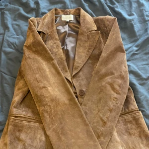 Brun skinnkavaj från Cappuccini - Säljer en snygg brun kavaj i 100% äkta skinn från Cappuccini. Den har en klassisk design med knappar framtill och fickor på sidorna. Perfekt för höst och vår när du vill ha en stilren look. Passar både till vardags och fest!