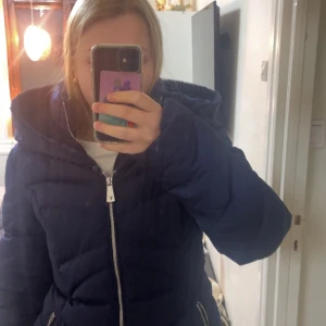 Mörkblå dunjacka från Guess - Säljer en snygg mörkblå dunjacka från Guess i nytt skick. Jackan har en mysig huva och stängs med dragkedja samt päls om man vill ha det. Perfekt för kalla vinterdagar! 💙