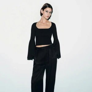 Svart trumpetärm topp - Snygg svart topp med långa ärmar och en fyrkantig halsringning. Perfekt för en stilren look, oavsett om det är till vardags eller fest. Den har en elegant och modern design som passar till många olika outfits.