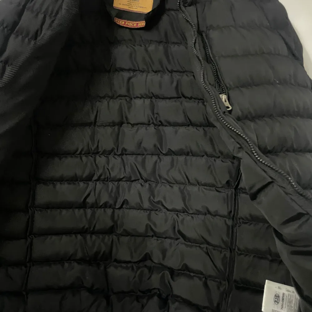 Säljer en snygg svart dunjacka från Parajumpers i mycket bra skick. Jackan är quiltad och har en dragkedja framtill. Perfekt för höst och vinter, med en normal passform och långärmade ärmar. Märkeslogga på ärmen ger en extra touch av stil. Perfekt för att hålla sig varm och trendig!. Takit.