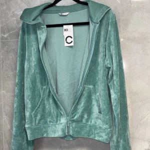 Grön velourjacka med dragkedja - Snygg och bekväm grön velourjacka med dragkedja framtill. Jackan har en huva och långa ärmar, perfekt för en avslappnad stil. Den mjuka velouren ger en lyxig känsla.