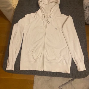 Vit hoodie med dragkedja - Säljer en stilren vit hoodie med dragkedja och fickor framtill. Perfekt för en avslappnad look. Den har en klassisk design med huva och långa ärmar.