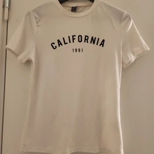 Vit t-shirt med tryck 'California 1991' - Snygg vit t-shirt med svart text 'California 1991' på framsidan. Perfekt för en avslappnad stil. Kortärmad och i mjukt material. Helt ny har inte använt än. Storlek 36 motsvarar S