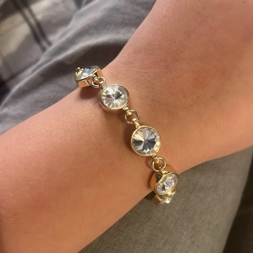 Elegant guldarmband med stora, klara kristaller infattade i guldfärgade länkar. Aldrig använd. Armbandet har en justerbar kedja och en säker klolås. Perfekt för att ge en glittrig touch till din outfit.. Asusteet.