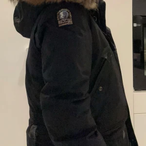 Svart parkajacka från Parajumpers - Snygg svart jacka från Parajumpers med pälsdetaljer på huvan. Jackan har långa ärmar och praktiska fickor framtill. Perfekt för kyliga dagar med sin varma och skyddande design. Denna jackan är använd ca 1 vinter och har därefter inte använts något. Jackan är köpt på barnavdelningen i NK, Göteborg. Det är en storlek S men jag skulle nog säga att den passar M också. Endast seriösa köpare! 