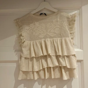 Populär volangtopp från Zara - Charmig beige topp från Zara med volanger och spetsdetaljer. Toppen är ärmlös och har en rund halsringning. Perfekt som festtopp eller finare tröja!! Tröjan är i storlek M men passar som S. 💘💘💘