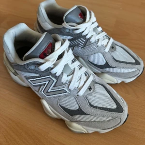 New Balance 9060 sneakers - Säljer ett par stilrena New Balance sneakers i grått och vitt. Skorna har en klassisk design med snörning och en bekväm sula. Perfekta för både vardag och träning. Storlek 37,5. Nya
