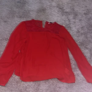 Röd blus med spetsdetaljer - Säljer en snygg röd blus med spetsdetaljer upptill. Blusen har långa ärmar och en elegant design som passar perfekt för olika tillfällen. Perfekt för den som vill ha något stilrent och bekvämt.