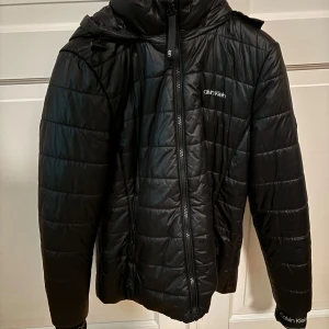 Svart pufferjacka från Calvin Klein - Snygg svart pufferjacka från Calvin Klein med dragkedja och huva. Super snygg o enkel vinterjacka!