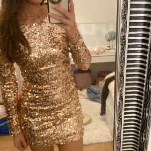 Guldig paljettklänning - Snygg och glittrig guldig paljettklänning med långärmad design och en öppen rygg. Perfekt för att sticka ut på festen! Pris kan diskuteras vid snabb affär.