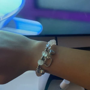 Armband med pärlor och hjärtberlocker - Snyggt armband med vita pärlor och silverfärgade hjärtberlocker. Perfekt accessoar för att ge en elegant touch till din outfit. Passar både till vardag och speciella tillfällen.