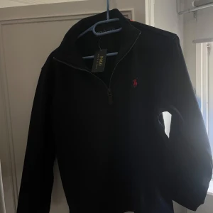  Polo Ralph Lauren tröja  - Snygg mörkblå tröja från Polo Ralph Lauren med dragkedja och det klassiska logotypbroderiet i rött på bröstet. Perfekt för en stilren look.
