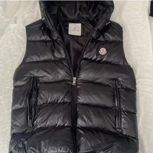 Svart dunväst från Moncler - Snygg svart dunväst från Moncler med dragkedja och huva.Har använts några gånger, inga skador, ren och säljer pågrund av att jag vill köpa en annan model, skicka prisförslag eller kontakta så kan vi snacka om pris eller om mer information och bilder