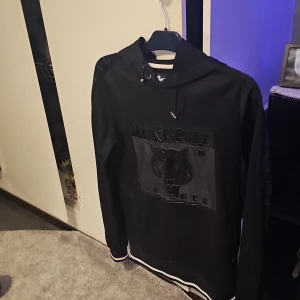 Svart hoodie från Plein Sport - Snygg svart hoodie från Plein Sport med ett stort tryck på framsidan. Den har en justerbar huva och ribbade muddar vid ärmslut och nederkant. Top skick inga fläckar eller märken 