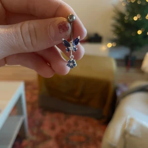 Blått navelpiercingsmycke med fjäril - Snyggt navelpiercingsmycke i silver med en glittrig blå fjäril och en hängande blå sten. Perfekt för att ge en extra touch till din stil. Passar utmärkt för både vardag och speciella tillfällen.