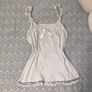 Vit ribbad linnetopp med spetsdetaljer - Jätte gulligt vitt linne med rosett på 🎀 Köpte den secondhand så står ej vart den är ifrån samt vad det är för storlek, jag säljer den då den är för stor på mig, skulle gissa att det är mellan S/M storlek 🤍Knappt använt den men eftersom den är secondhand så kan man se att det vita färgen börjat ”fadeat”.