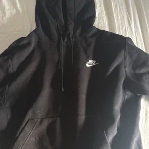 Svart hoodie från Nike - Säljer en klassisk svart hoodie från Nike med vit logga på bröstet. Den har en justerbar huva och en stor ficka framtill. Storlek S men är stor i storleken så passar även M kanske L. 