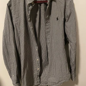 Rutig skjorta från Ralph Lauren - Snygg rutig skjorta från Ralph Lauren i svart och vit. Skjortan har långa ärmar och klassisk krage med knappar framtill. Perfekt för en stilren look. Mycket fint skick, storlek : S