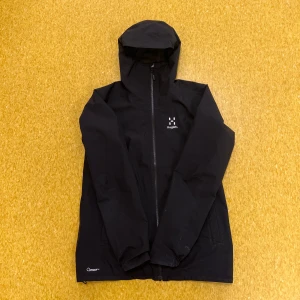 Haglöfs Vind/Regn - jacka - Haglöfs Vindjacka/Regnjacka 	•	Färg: Svart 	•	Storlek: S för män (passar även kvinnor i storlek M) 	•	Perfekt för vindiga och regniga dagar 	•	Köpt i början av hösten 2024 för 2220 kr 	•	Nuvarande pris: 1600 kr (pris kan diskuteras!!)  Jackan är i nyskick, endast använd ett par gånger. Säljes på grund av oanvändning. Ett funktionellt och stilrent plagg för alla väder! Hör av dig vid intresse.