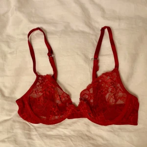 Röd spets-bh 75B - Spänne för att hålla ihop axelbanden i brottarrygg. Oklart märke då lappen inte finns kvar. 