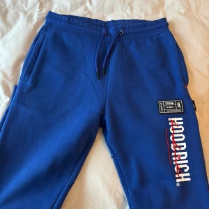 Blå mjukisbyxor från Hoodrich - Snygga blå mjukisbyxor från Hoodrich med tryck i vitt och rött. Byxorna har snörning i midjan och elastiska muddar vid bensluten. Inte använda mer än 2 gånger!