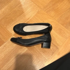 Svarta ballerinaskor med klack - Snygga svarta ballerinaskor i skinn med låg klack och en liten rosett. Från märket Clark. Står att st ska vara 4 1/2 vilket motsvarar 35 men jag som har st 37 kan inte ha dem. Det går säkert med en svart läderfärg att få bort defekten på hälen! Nypris är runt 800-1000