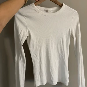 Vit ribbad långärmad topp - Säljer en stilren vit ribbad långärmad topp. Perfekt för lager-på-lager eller som den är. Enkel och mångsidig design som passar till det mesta. Hör av dig vid intresse!