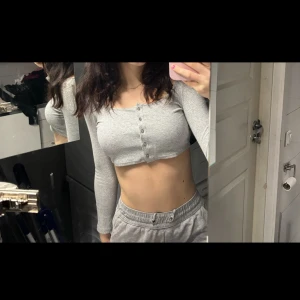 Grå croppad topp från H&M - Säljer en grå croppad topp från H&M med långa ärmar och knappar framtill. Perfekt för en avslappnad stil.