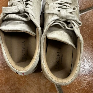 Beige sneakers från Les Deux - Snygga beige sneakers från Les Deux med snörning och diskreta detaljer i rött, vitt och blått på hälen. Perfekta för en stilren look.