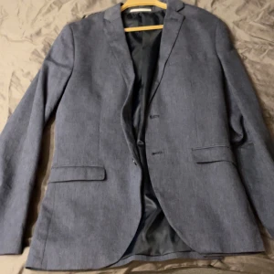 Blå kavaj och byxor - Snygg blå kavaj med matchande byxor . Byxorna har en enkel design med knapp och dragkedja. Perfekt för en stilren look. Passar dom som är 170 till 175 bäst 