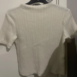 Vit ribbad topp från Zara - Säljer en stilren vit ribbad topp från Zara. Toppen har korta ärmar och en klassisk passform som passar perfekt till vardags.