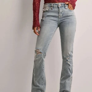 Ljusa bootcut jeans från True Religion - Snygga ljusa bootcut jeans från True Religion med slitningar på knäna, köpta från Nelly. Men De har en midwaist passform, röda detaljer och de är modell Becca. Storlek 27, passar mig som är 172 cm. Säljer pga dem är för stora i midjan för mig. Använda få gånger, har dock en liten fläck vid foten av byxan som ej går bort (se sista bilden). 