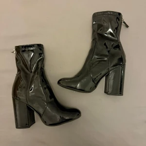 Svarta lackade stövletter med klack - Snygga svarta stövletter i lackat material med hög klack och dragkedja baktill. Perfekta för en stilren look.
