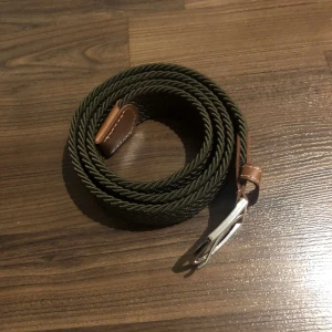 Flera flätade bälten i olika färger - Säljer ett set av flätade bälten i olika färger: grönt, blått, svart, vitt, beige och svartvitt mönster. Bältena har detaljer i brunt läder och en stilren design med metallspänne. Perfekt för att ge din outfit en extra touch!