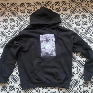 Svart hoodie med tryck - Säljer en svart hoodie med en stor ficka fram och ett tryck av Virgil Abloh på bröstet. Perfekt för en avslappnad stil. Bra skick då den är varsamt använd