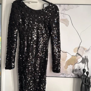 Svart paljettklänning - Snygg svart klänning från NLY One täckt med glittrande paljetter. Den har en figurnära passform och långa ärmar, perfekt för en festlig kväll. Klänningen är tillverkad i ett bekvämt material som ger en lyxig känsla.