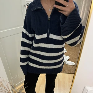 Randig stickad tröja med dragkedja - Mysig blå och vit randig stickad tröja med dragkedja och krage. Perfekt för kyliga dagar med sin avslappnade passform och långa ärmar.