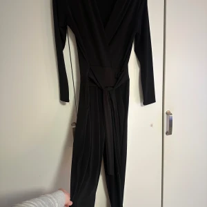 Svart långärmad jumpsuit - Elegant svart långärmad jumpsuit med omlott-design och knytband i midjan