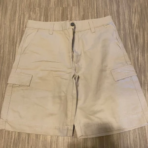Beige cargo shorts - Snygga beige cargo shorts med praktiska fickor på sidorna och dragkedja framtill. Perfekta för en avslappnad stil.
