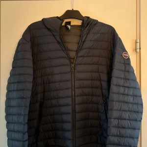 Mörkblå dunjacka från Colmar - Snygg mörkblå dunjacka från Colmar med huva och dragkedja. Jackan har ett quiltat mönster och en rund logotyp på ärmen. Perfekt för kyliga dagar.