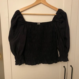 Svart offshoulder topp - Snygg svart offshoulder topp med puffiga ärmar och smockdetaljer. Perfekt för en stilren look med en touch av elegans. Passar bra till både jeans och kjol. Du kan både bära den som den är på bilden eller som en off shoulder topp💕