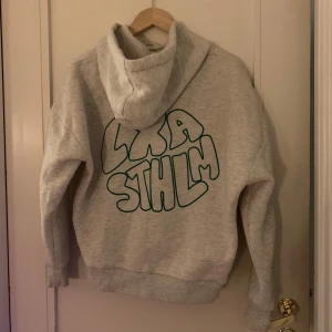 Grå LXA hoodie XS - Slutsåld grå hoodie från LXA i storlek XS. Grön text på ryggen. Köpt av en tjej här på Plick men tyvärr för liten för mig ❤️