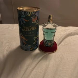 Jean Paul Gaultier Le Beau Parfum 125ml - Säljer en elegant parfymflaska från Jean Paul Gaultier, Le Beau Parfum. Flaskan har en unik kroppsliknande form i transparent glas med en ljusblå vätska. Den kommer i en stilren, mönstrad förpackning med tropiska inslag. Perfekt för den som vill ha en doft med karaktär och stil. De är ungefär 100 ml kvar.